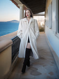 Woman in a white coat standing on a balcony with a scenic ocean view.