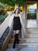 Woman in a black dress and white fur coat standing on steps with a scenic background