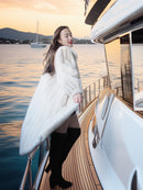Woman in a white coat standing on a yacht with a scenic water background
