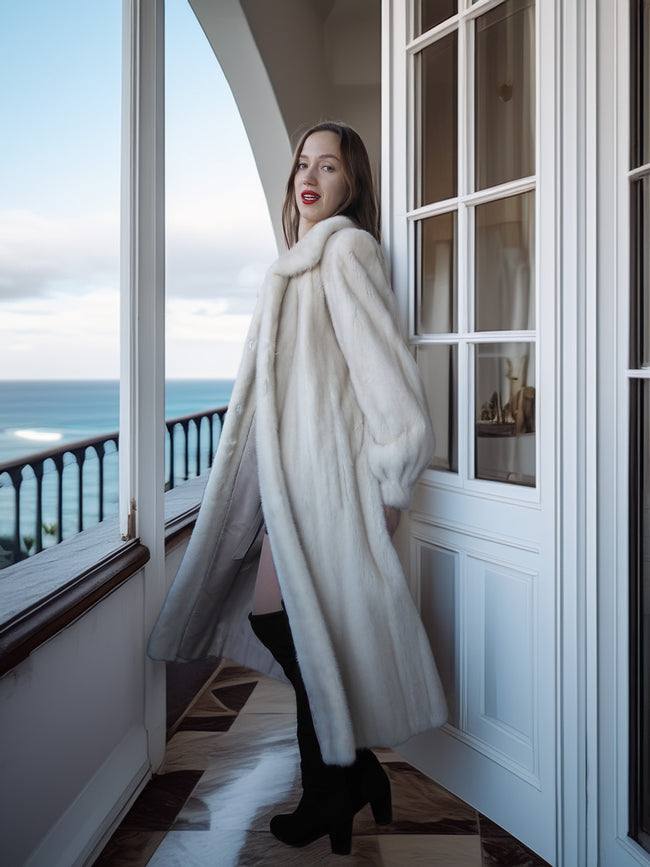 Woman in a white fur coat standing on a balcony with ocean view