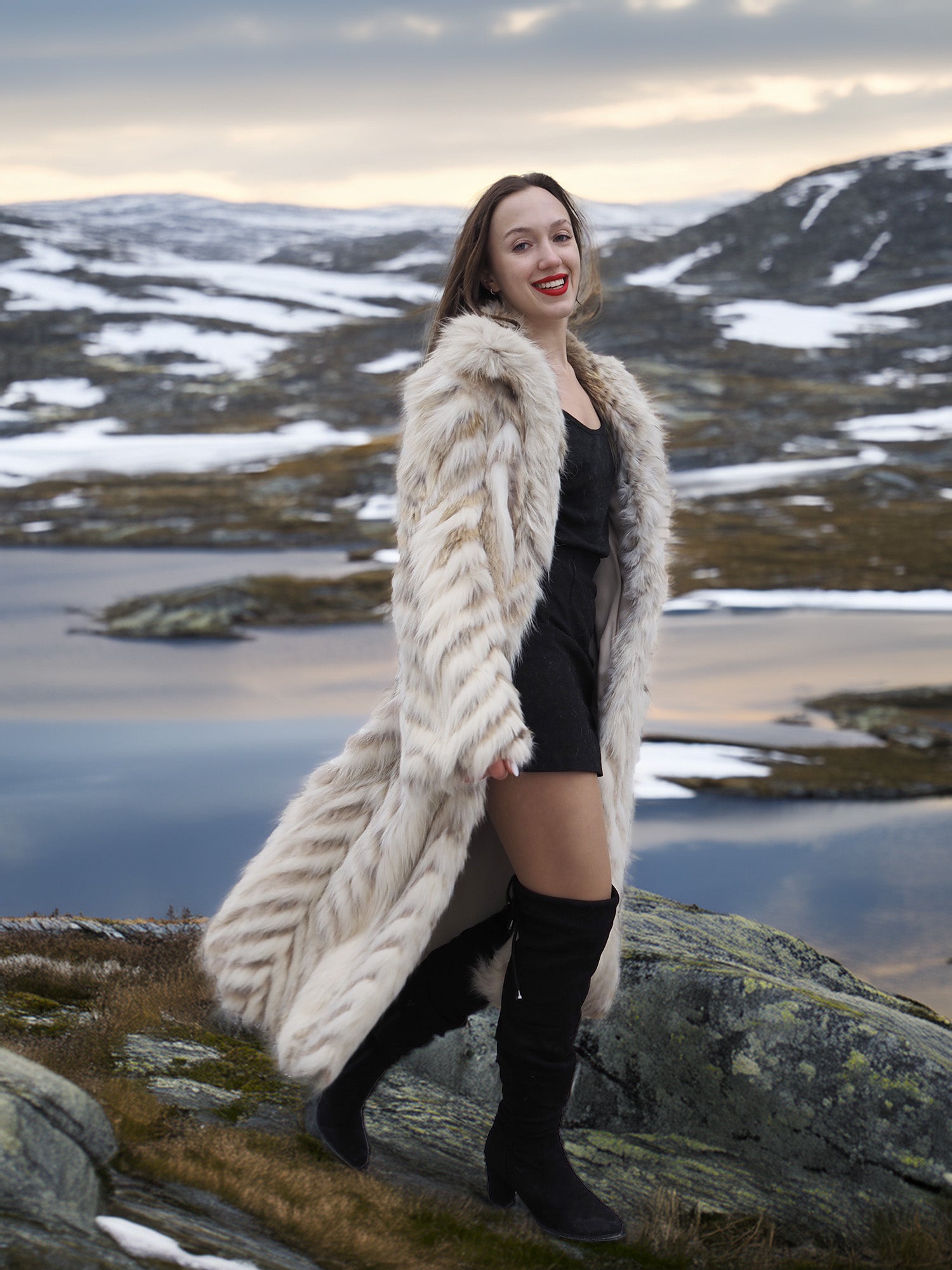 Model smiling in Two Tone Fox Coat Size XS/S with chevron fur pattern, styled in a rocky winter landscape for chic outerwear fashion.