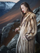 Woman wearing a fur coat standing on a rocky landscape with a dramatic sky.