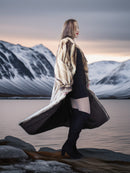 Person wearing a fur coat standing on a rocky landscape with mountains in the background