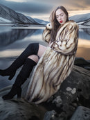 Woman in fur coat and black boots sitting on a rock with a scenic background