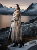Woman in a fur coat standing in a snowy landscape with mountains in the background