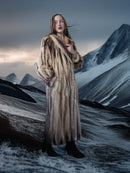 Person wearing a fur coat standing in a snowy mountain landscape