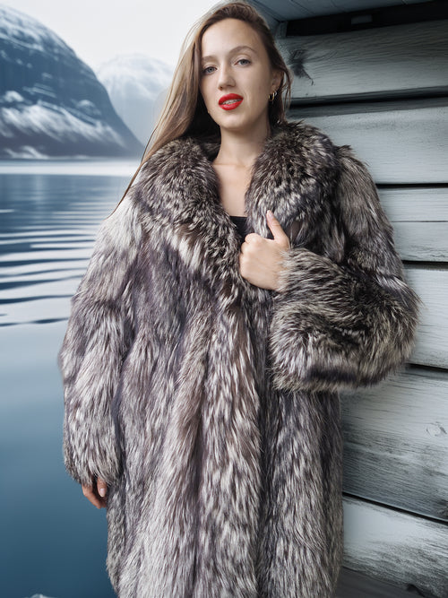 Woman wearing a fur coat by a body of water with mountains in the background