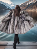 Person wearing a large fur coat standing on a dock with mountains and water in the background