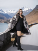 Woman in a fur coat and black dress standing in front of mountains and water