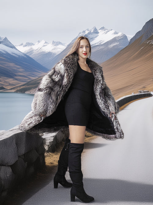 Woman in a fur coat and black dress standing in front of mountains and water
