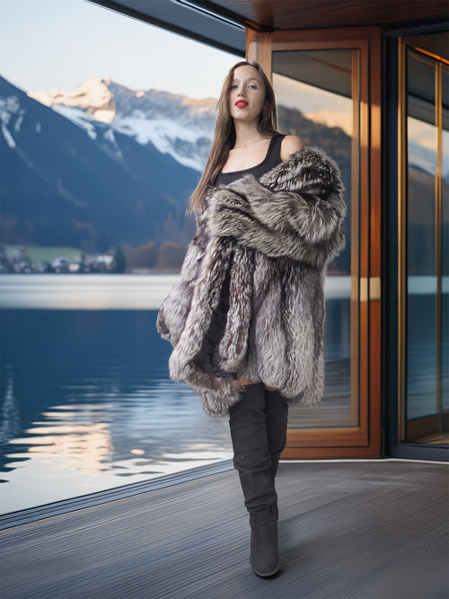 Woman in a fur coat standing in front of a large window with a mountain view.