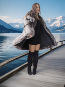 Woman in a fur coat and black dress standing on a dock with mountains and lake in the background