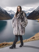 Person wearing a fur coat standing on a road with mountains and a lake in the background
