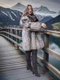 Woman in a fur coat standing on a wooden bridge with mountains in the background