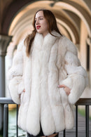 Woman wearing a white fur coat standing in front of an architectural background