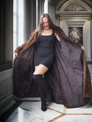 Woman in a black dress and fur coat standing in an elegant interior setting.