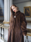Woman wearing a long brown fur coat in an elegant interior setting.
