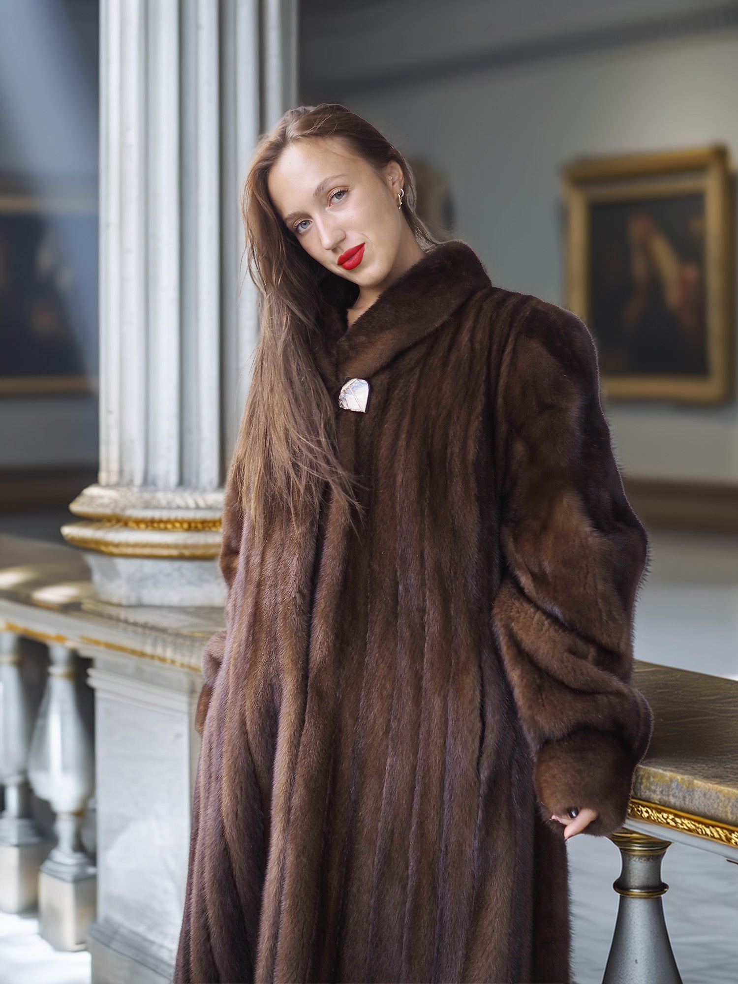 Woman wearing a long brown fur coat in an elegant interior setting.