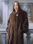 Woman wearing a long brown fur coat in an elegant interior setting.