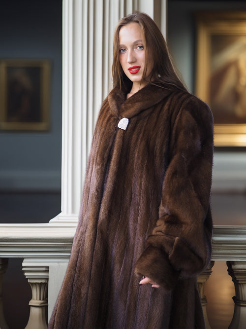 Woman wearing a long brown fur coat indoors with decorative elements in the background