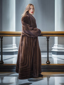 Woman wearing a long brown fur coat in an elegant interior setting with columns.