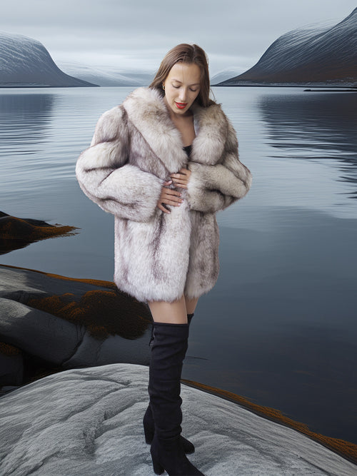 Woman in a fur coat standing on a rocky outcrop with a lake and mountains in the background