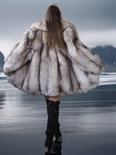 Person wearing a fur coat walking on a beach with mountains in the background