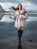Woman in a fur coat standing on a reflective beach with mountains in the background