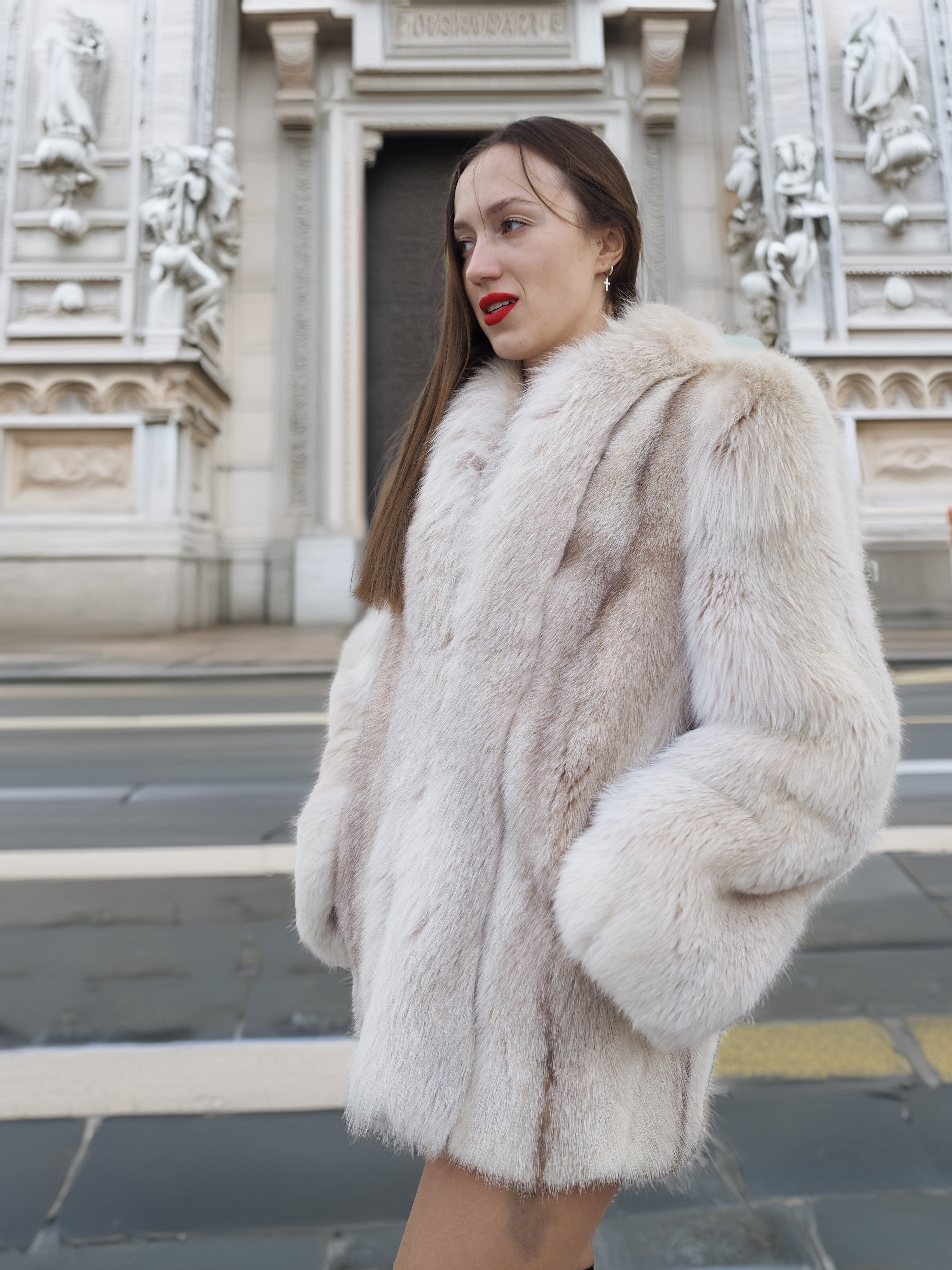 Side view of Brown Cross Mink Fur Coat Jacket S with Blush Fox Trim in front of historic architecture, showcasing timeless elegance and warmth.