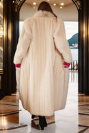 Person wearing a long cream fur coat in a stylish interior setting