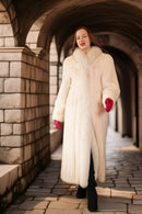 Woman in a long white fur coat standing in an archway.