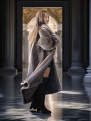 Woman in a fur coat standing in a grand hallway with columns.