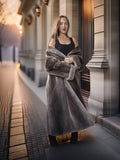 Woman in a long fur coat standing on a city street at night.