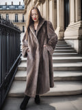 Woman wearing a long brown coat standing on steps in an urban setting