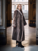 Woman wearing a long fur coat standing in an elegant interior setting.