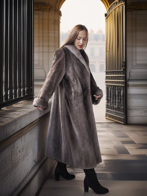 Woman in a long gray coat standing in an elegant interior setting.