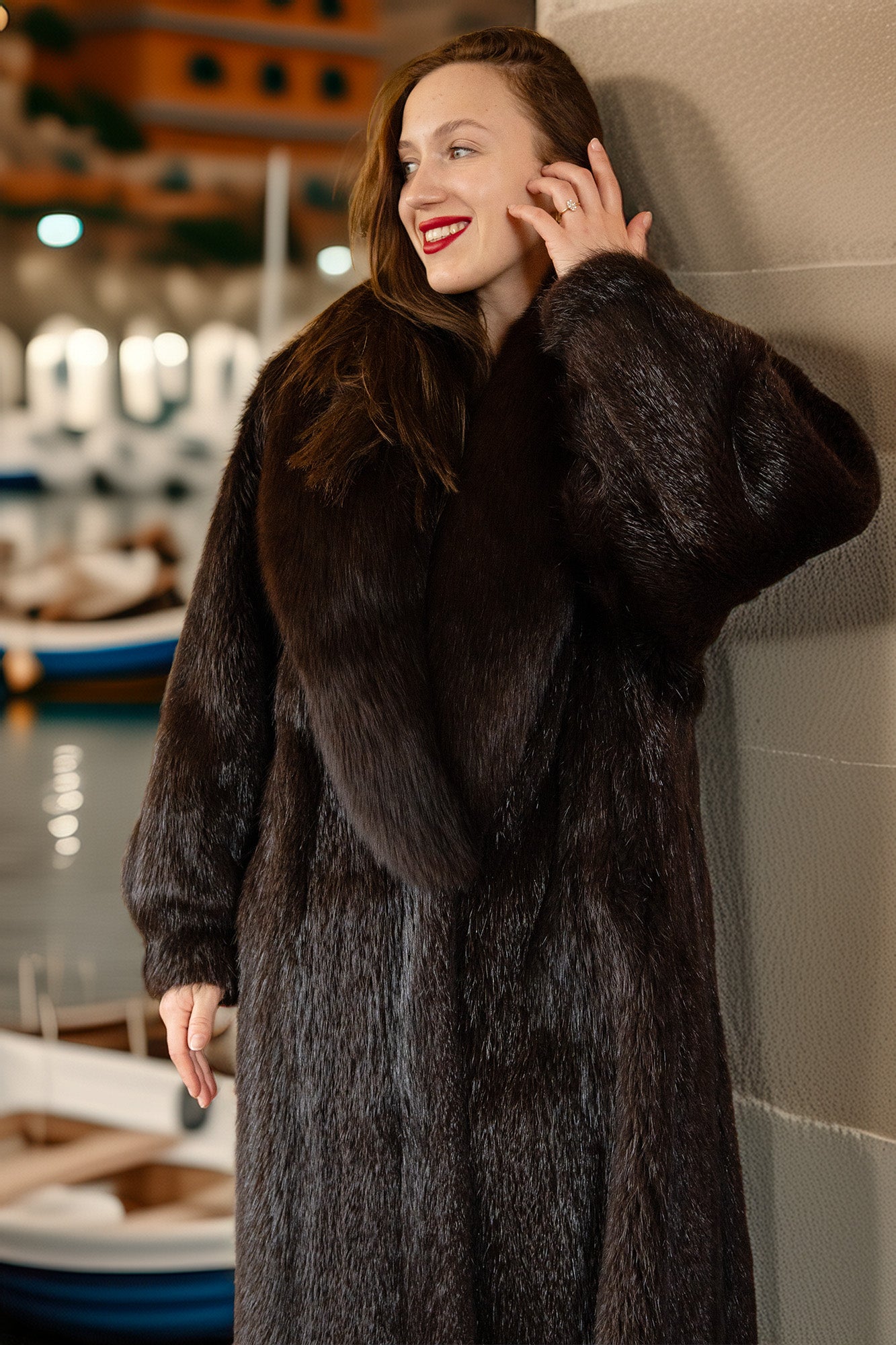 Woman wearing a fur coat leaning against a wall indoors.