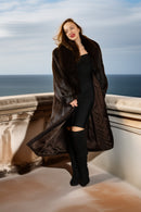 Woman in a long dark coat standing on a balcony with ocean view