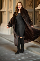 Woman wearing a long brown fur coat and black dress with knee-high boots in an elegant setting.