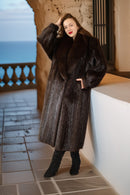 Woman wearing a fur coat standing on a balcony with a scenic view.