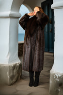 Person wearing a long brown fur coat standing on a stone path with columns.