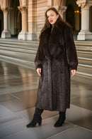 Woman wearing a long dark fur coat standing in an architectural setting.