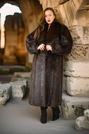 Woman wearing a fur coat standing in front of stone ruins