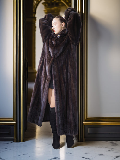 Person wearing a long brown fur coat in an elegant interior setting.