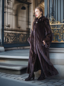Woman in a long dark fur coat standing in front of an ornate door.