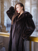 Woman wearing a dark fur coat standing indoors with a blurred background