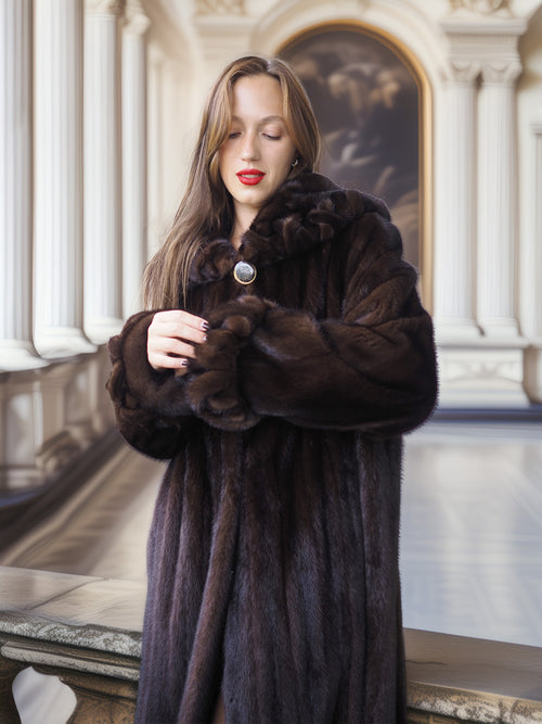Woman wearing a long brown fur coat indoors.