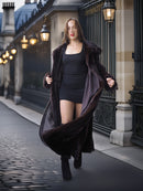 Woman in a long dark coat walking on a city street with classical architecture.
