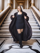 Woman in a long dark coat standing on a grand staircase with classical architecture.