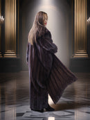 Woman in a long fur coat standing in an elegant room with chandeliers.
